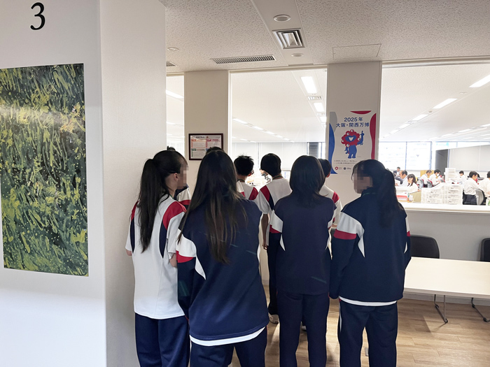 机を囲んで業務改善グッズを見る社員と中学生